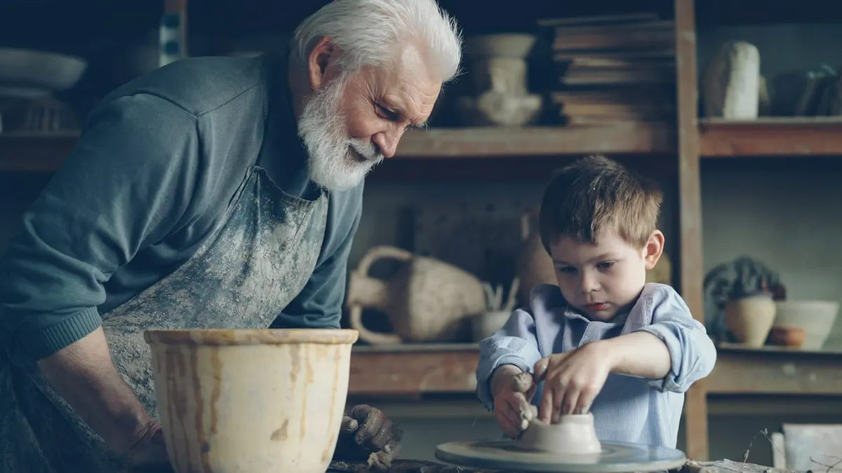 A grandfather and a boy shaping clay at a pottery wheel
