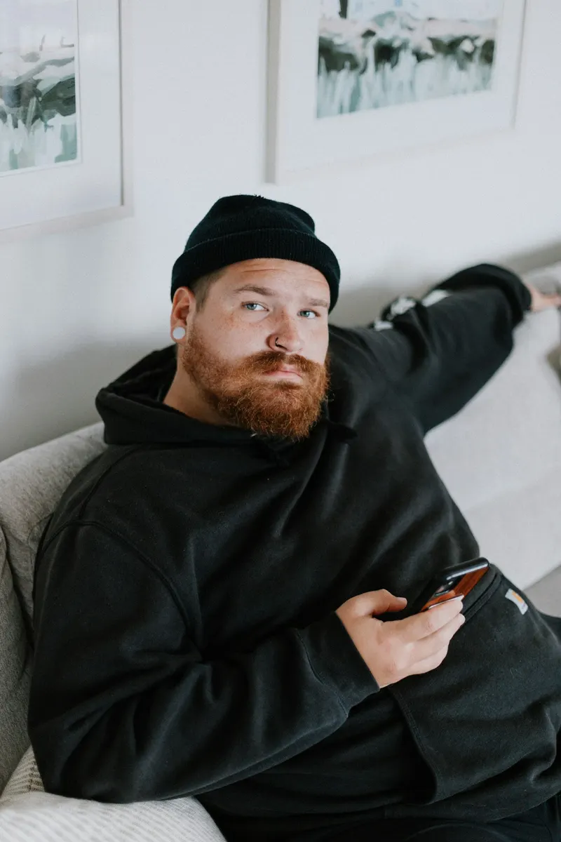 A bearded man in a beanie sitting on a couch